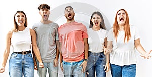 Group of young friends standing together over isolated background angry and mad screaming frustrated and furious, shouting with