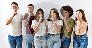 Group of young friends standing together over isolated background asking to be quiet with finger on lips