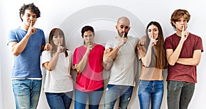 Group of young friends standing together over isolated background asking to be quiet with finger on lips