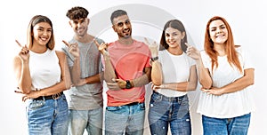 Group of young friends standing together over isolated background with a big smile on face, pointing with hand finger to the side