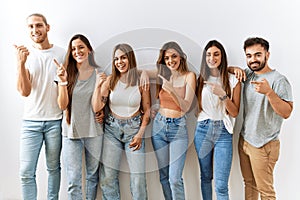 Group of young friends standing together over isolated background cheerful with a smile on face pointing with hand and finger up