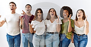 Group of young friends standing together over isolated background crazy and mad shouting and yelling with aggressive expression