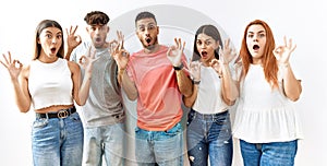Group of young friends standing together over isolated background looking surprised and shocked doing ok approval symbol with