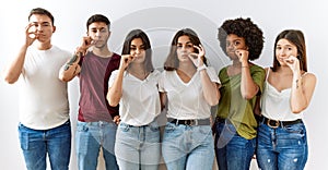 Group of young friends standing together over isolated background mouth and lips shut as zip with fingers