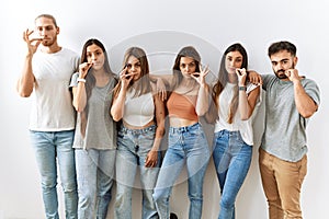 Group of young friends standing together over isolated background mouth and lips shut as zip with fingers