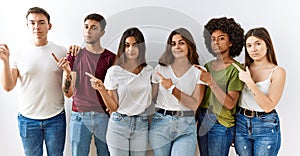 Group of young friends standing together over isolated background pointing with hand finger to the side showing advertisement,