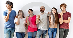 Group of young friends standing together over isolated background smiling with happy face looking and pointing to the side with