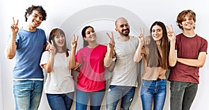 Group of young friends standing together over isolated background smiling looking to the camera showing fingers doing victory sign