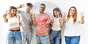 Group of young friends standing together over isolated background smiling with tongue out showing fingers of both hands doing