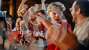 Group of Young Friends Watching a Live Soccer Match on TV in a Sports Bar. Excited Fans Cheering and