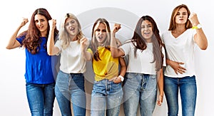 Group of young girl friends standing together over isolated background angry and mad raising fist frustrated and furious while