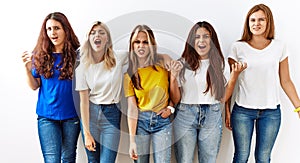 Group of young girl friends standing together over isolated background angry and mad screaming frustrated and furious, shouting