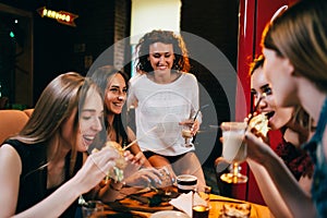 Group of young girlfriends having lunch in fast food restaurant eating craft hamburgers