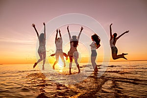 Group of young girls jumps at sunset beach