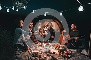 Group of young happy friends having picnic outdoors with sparklers