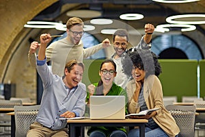 Group of young happy multiracial business people sitting at desk in the modern office or coworking space, looking at photo