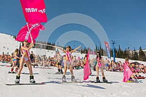 Group of young happy pretty women on a snowboard in colorful bikini with flags.