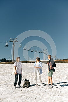 Group of young hikers with dog standing in the snow at a mountain resort on a sunny spring day and talking. Vertical