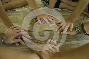 Group of young hipster American friends enjoying Asian yoga retreat together sitting on lotus position holding hands on wooden hut