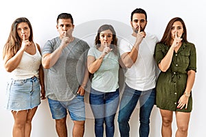 Group of young hispanic friends standing together over isolated background asking to be quiet with finger on lips