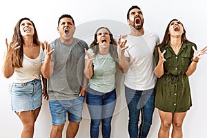Group of young hispanic friends standing together over isolated background crazy and mad shouting and yelling with aggressive