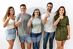 Group of young hispanic friends standing together over isolated background doing happy thumbs up gesture with hand