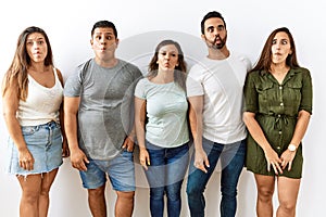 Group of young hispanic friends standing together over isolated background making fish face with lips, crazy and comical gesture