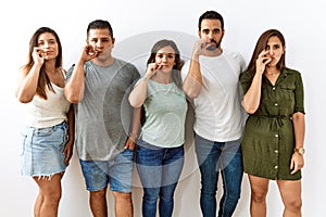 Group of young hispanic friends standing together over isolated background mouth and lips shut as zip with fingers