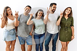 Group of young hispanic friends standing together over isolated background smiling looking to the camera showing fingers doing