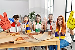 Group of young hispanic people eating pizza supporting soccer team at home celebrating victory with happy smile and winner