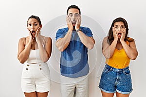 Group of young hispanic people standing over isolated background afraid and shocked, surprise and amazed expression with hands on