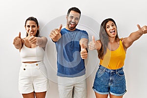 Group of young hispanic people standing over isolated background approving doing positive gesture with hand, thumbs up smiling and