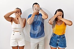 Group of young hispanic people standing over isolated background covering eyes and mouth with hands, surprised and shocked