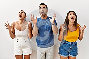 Group of young hispanic people standing over isolated background crazy and mad shouting and yelling with aggressive expression and