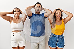 Group of young hispanic people standing over isolated background crazy and scared with hands on head, afraid and surprised of