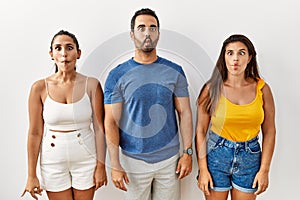 Group of young hispanic people standing over isolated background making fish face with lips, crazy and comical gesture