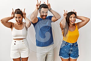 Group of young hispanic people standing over isolated background posing funny and crazy with fingers on head as bunny ears,