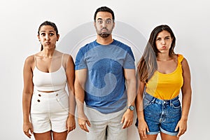 Group of young hispanic people standing over isolated background puffing cheeks with funny face