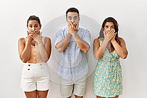 Group of young hispanic people standing over isolated background shocked covering mouth with hands for mistake