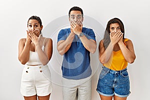 Group of young hispanic people standing over isolated background shocked covering mouth with hands for mistake