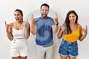 Group of young hispanic people standing over isolated background shouting with crazy expression doing rock symbol with hands up