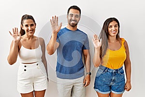 Group of young hispanic people standing over isolated background waiving saying hello happy and smiling, friendly welcome gesture