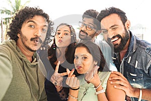 Group of young Indian friends taking selfie with grimacing faces by looking camera during reunion party - concept of