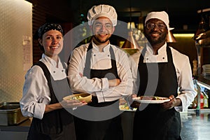 Group of young intercultural successful cooks in uniform looking at camera