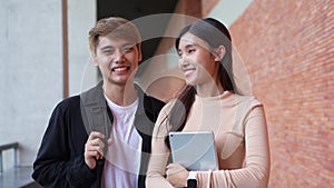 Group of young interracial diverse university students reading textbook and sitting outside a classroom under a building, engaging