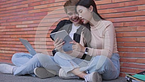 Group of young interracial diverse university students reading textbook and sitting outside a classroom under a building, engaging