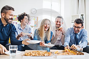 Group of young businesspeople with pizza having lunch in a modern office.