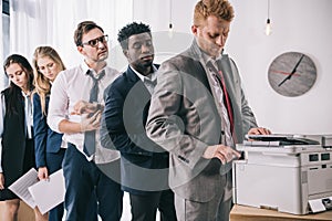 group of young managers standing in queue for copier