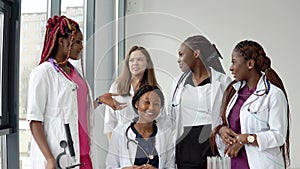 A group of young medics of different races sitting and standing at a table are having a conversation