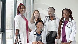 A group of young medics of different races sitting and standing at a table are having a conversation